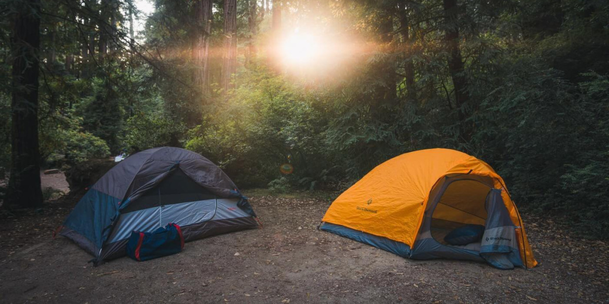 Two tents in the forest and the sun is shining through the leaves.